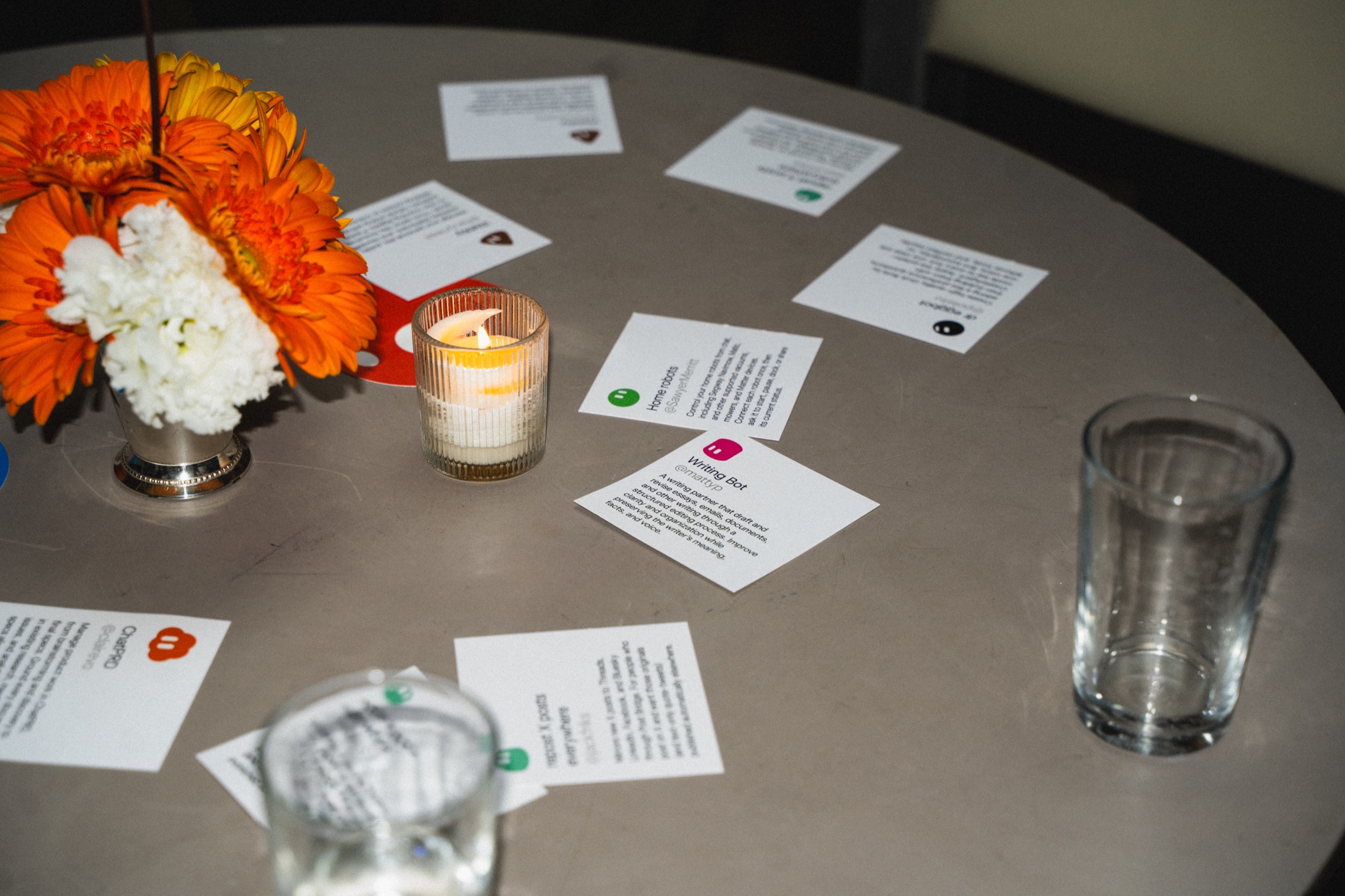 Printed bot cards, orange and white flowers, and a candle on a table at the New York event