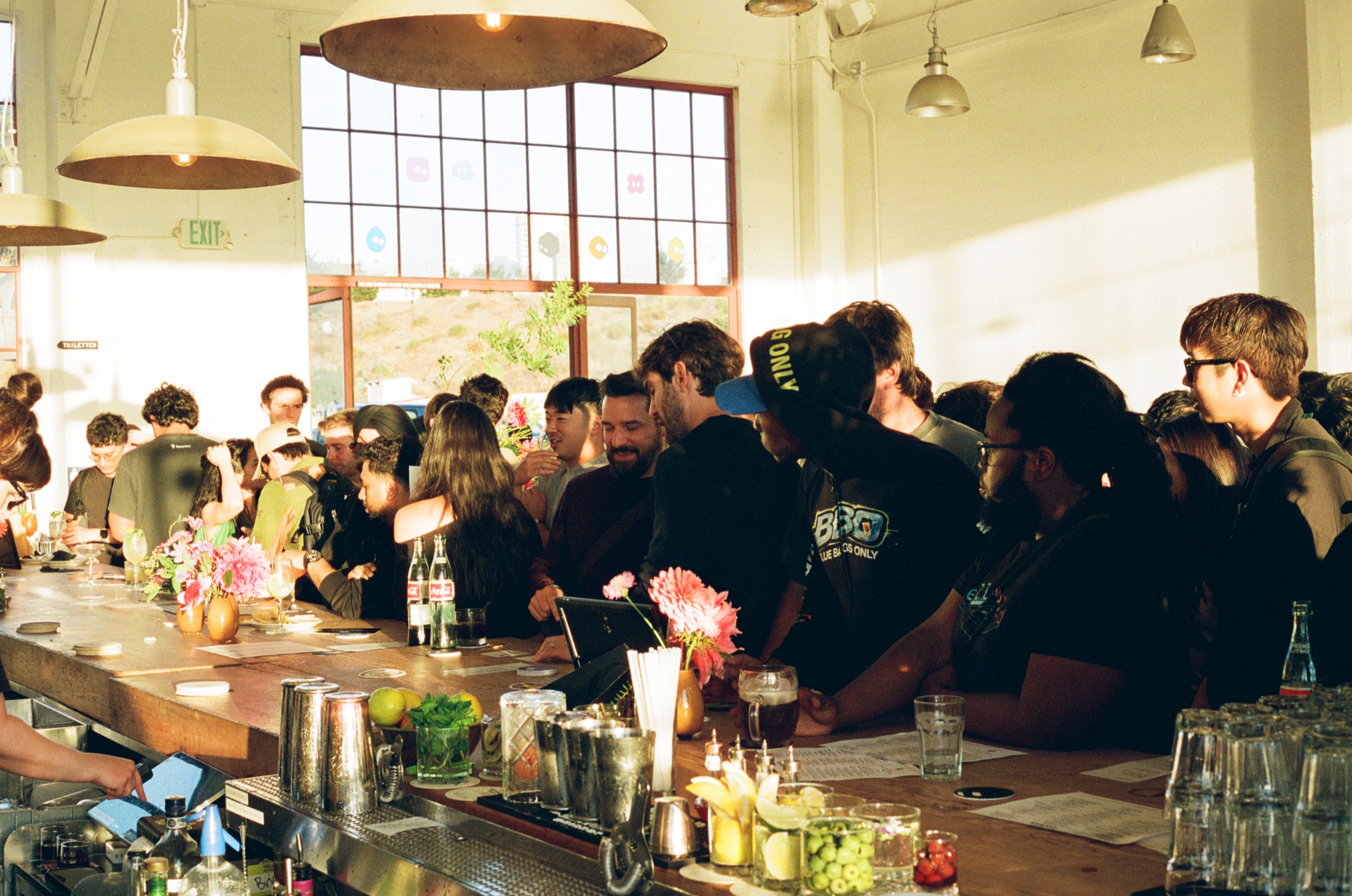 Guests gathered around the sunlit bar with pink flowers at Grok Builders Night in San Francisco