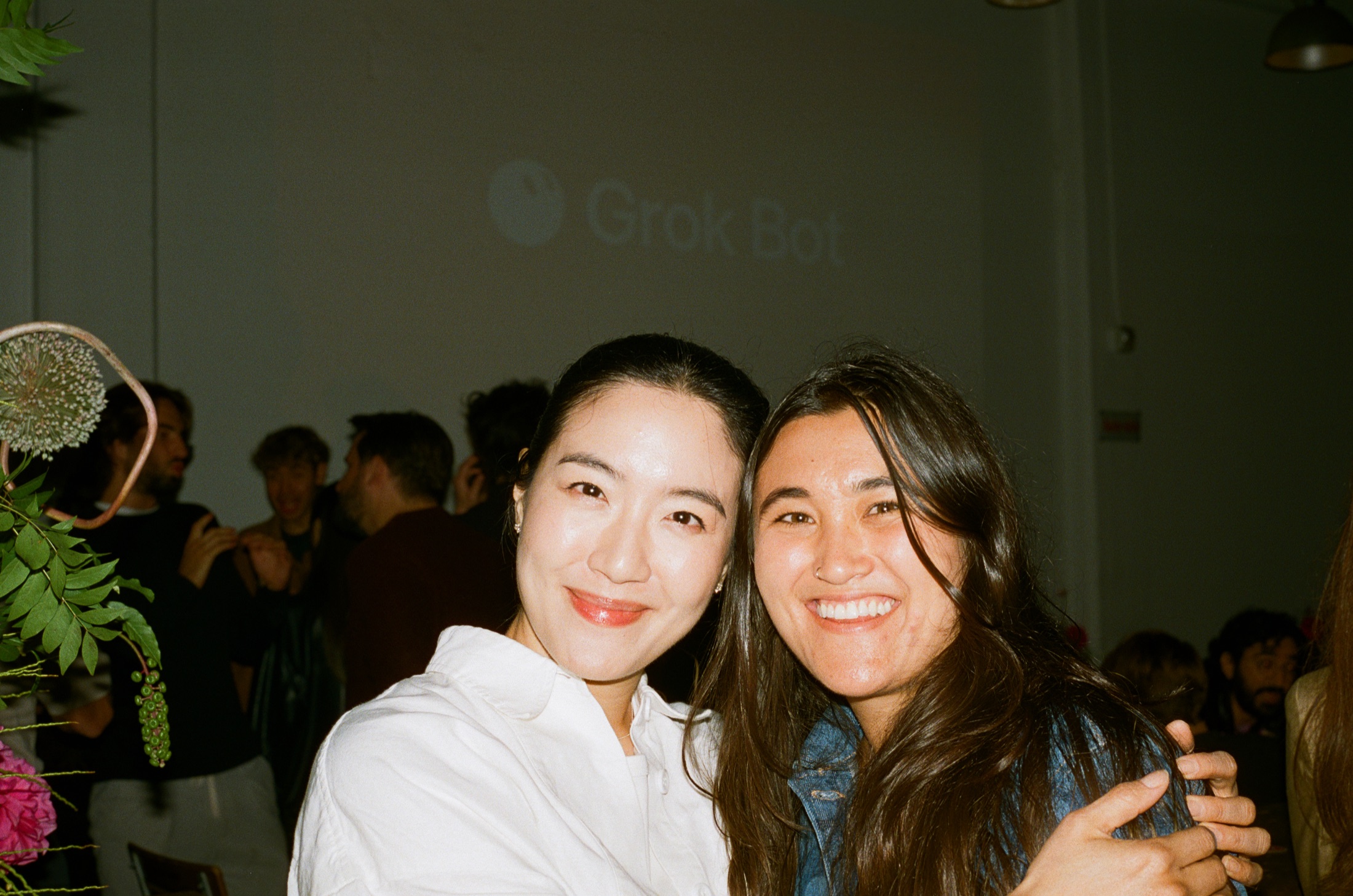 Two people posing for a photograph with the Grok Bot projection and event crowd behind them