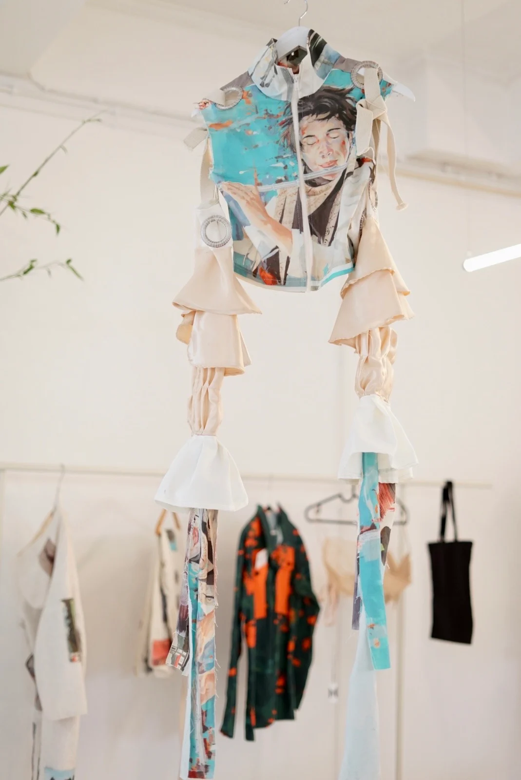 A suspended illustrated garment with turquoise panels and layered cream sleeves