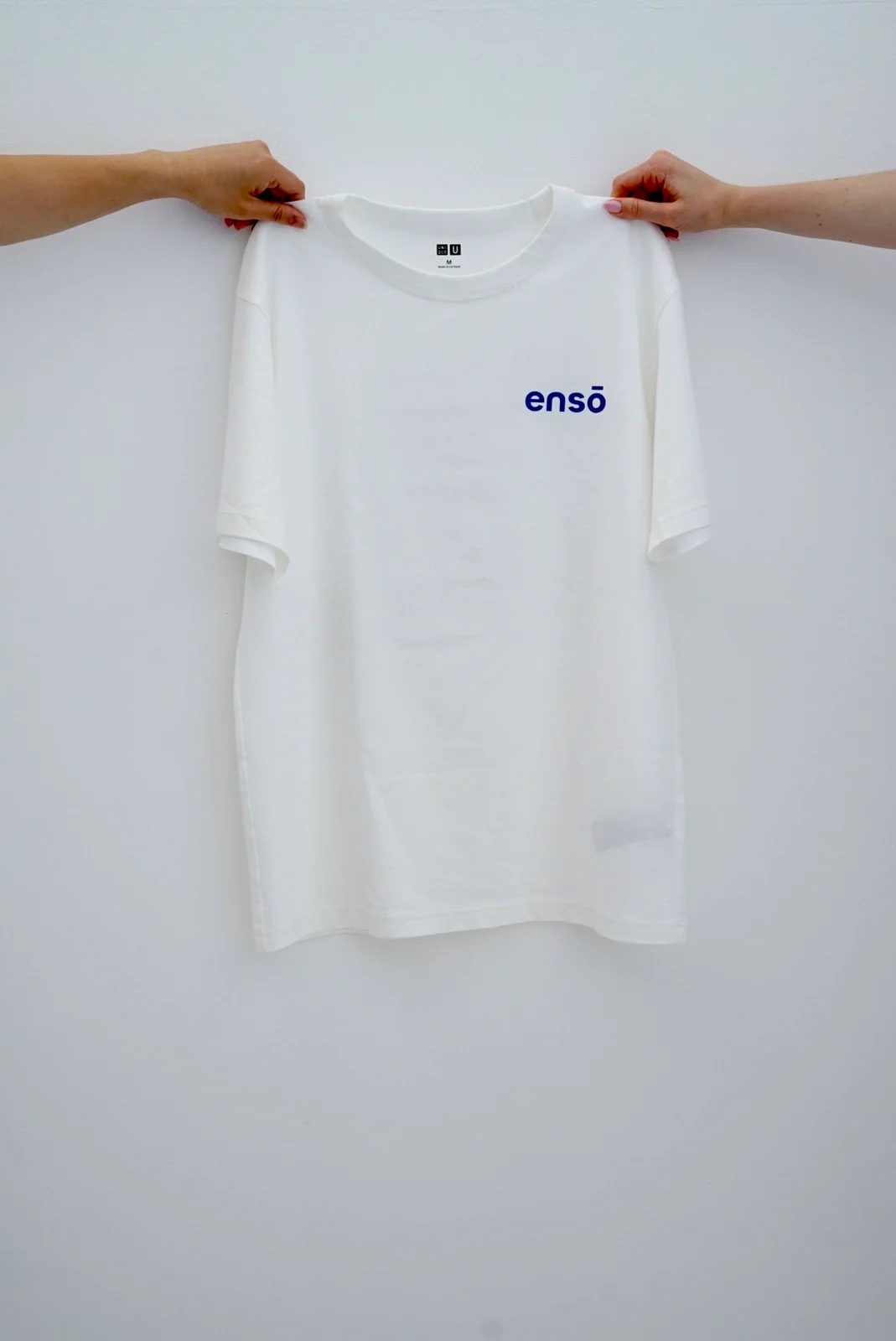 The front of a white Enso T-shirt with a small blue chest logo
