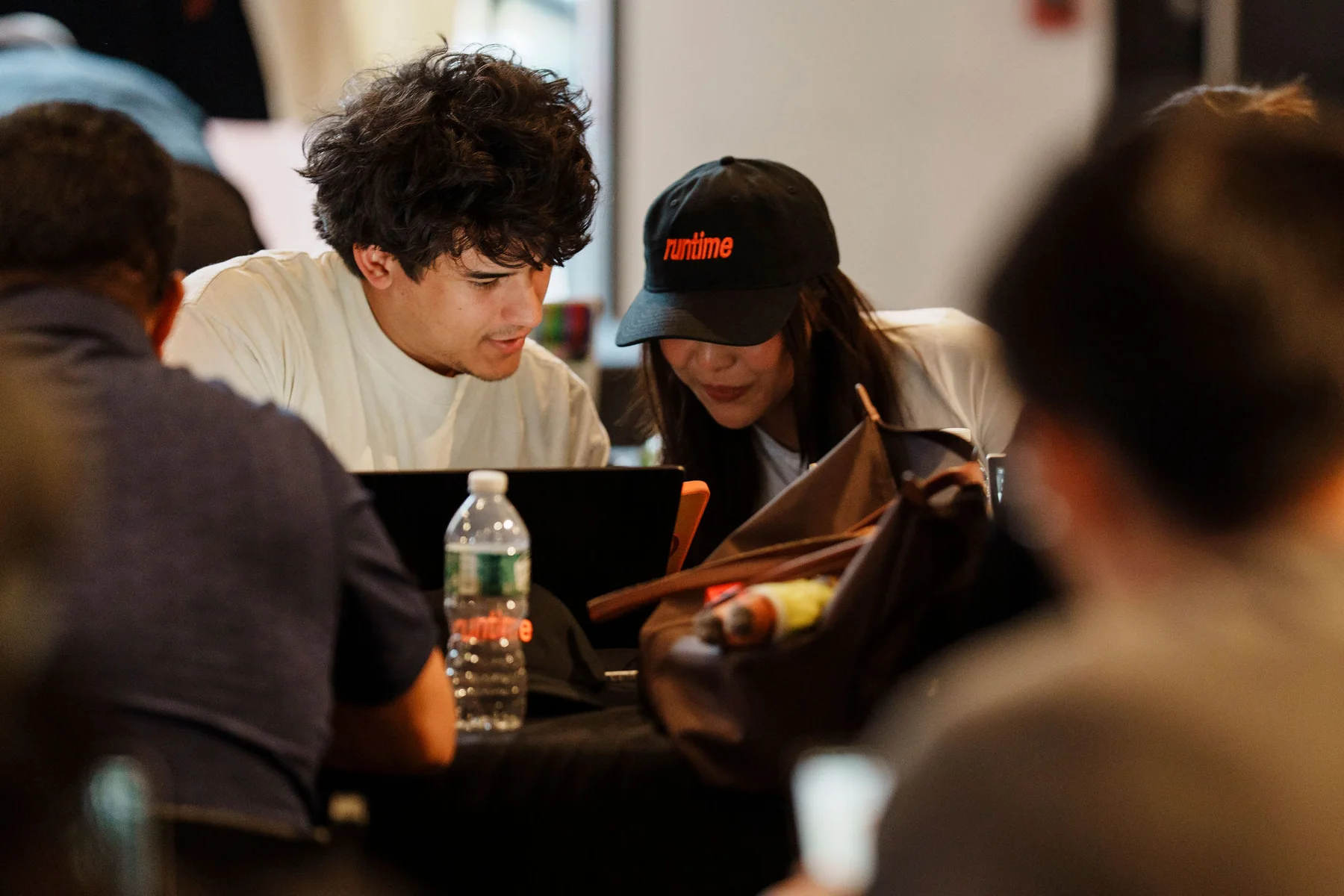 Participants collaborating over a laptop, one wearing a Runtime cap