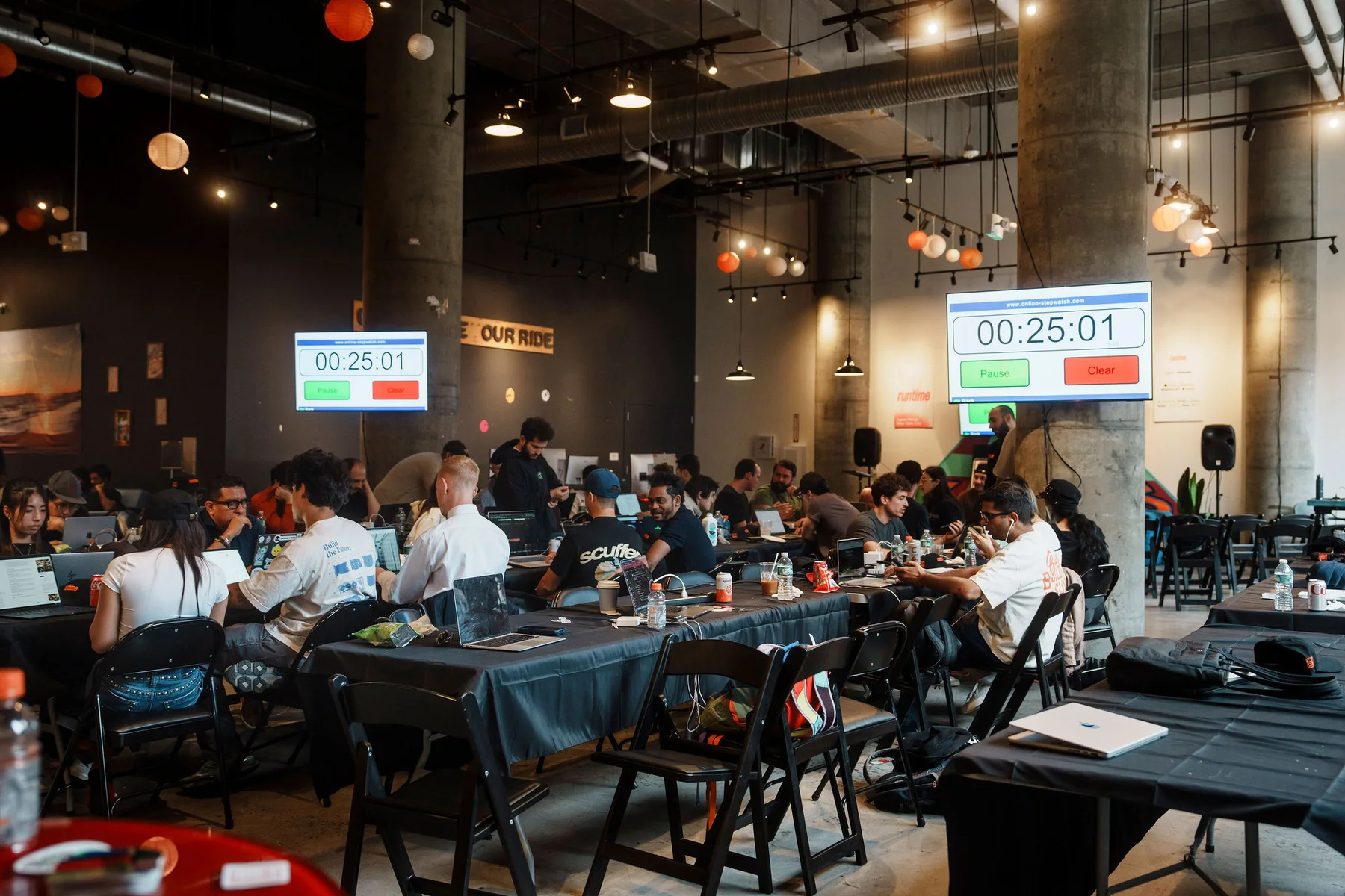 Hackathon participants working at tables beneath screens displaying a countdown